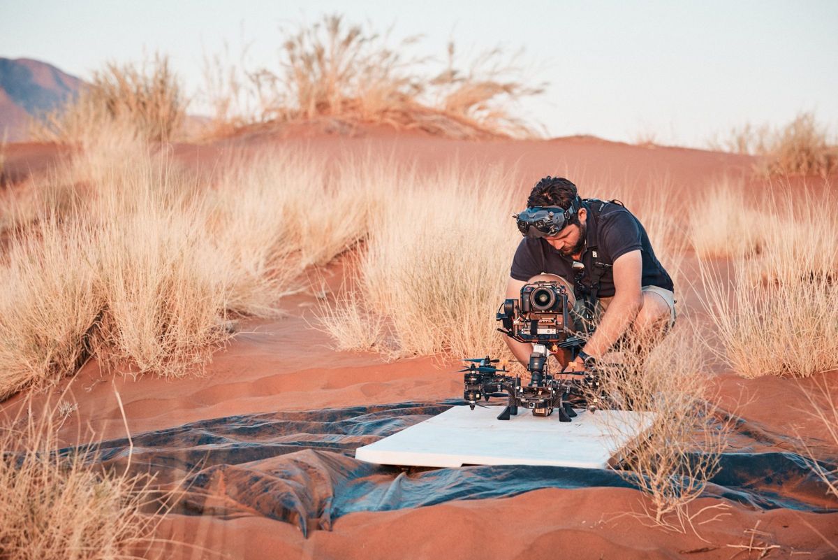 Filmic pilot Dimitri Vaindirlis rigging a gimbal stabilised FPV drone on a launch board in the red dunes of the Namib