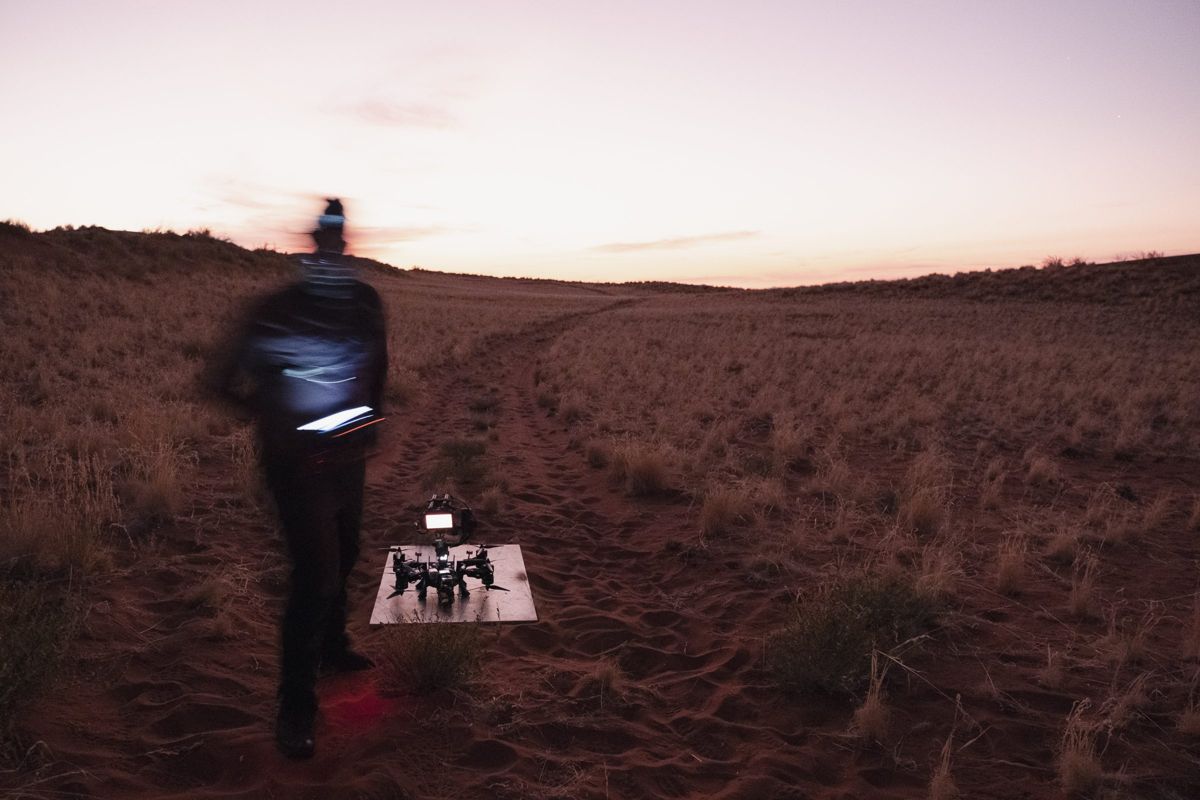Heavy lift drone on its launch pad at dusk in the Namib, pilot walking in